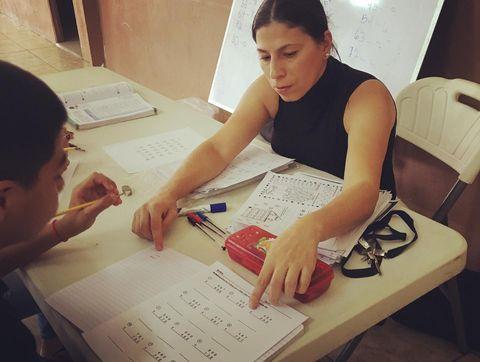 Tutor points finger at notebook to teach child.