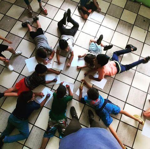 Aerial shot of children doing an activity with notebooks on the floor in a circle.